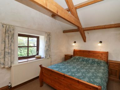 A bedroom with wooden bed frame and green bedspread next to a window and wooden beams at Cove Cottage in Llangrannog