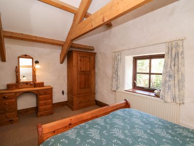 A bedroom with wooden beams wooden wardrobe wooden dressing table and a window with curtains at Cove Cottage in Llangrannog