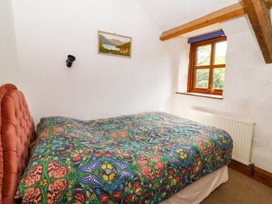 A bedroom with a bed with a butterfly patterned cover near a window with wooden beams at Cove Cottage in Llangrannog