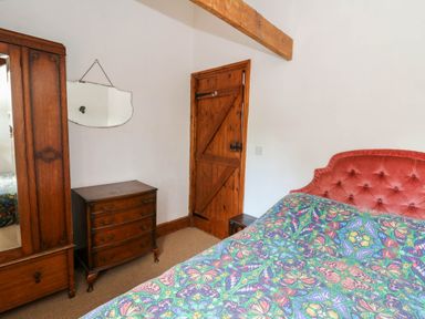 A bedroom with a wooden wardrobe chest of drawers mirror wooden door and a bed with butterfly patterned bedding at Cove Cottage in Llangrannog