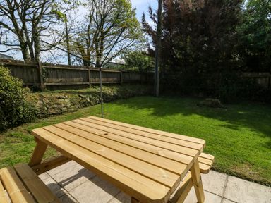 A wooden picnic table on a patio with a rotary clothesline and grass fenced garden at Cove Cottage in Llangrannog