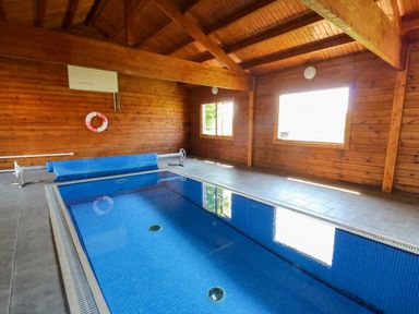An indoor swimming pool with blue tiles inside a wooden room with windows at Cove Cottage in Llangrannog