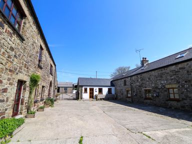A courtyard with stone buildings on both sides and a small white building at the end at Cove Cottage in Llangrannog
