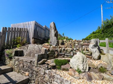 A stone bench and rock garden with wooden fencing and greenery in an outdoor setting at Cove Cottage in Llangrannog