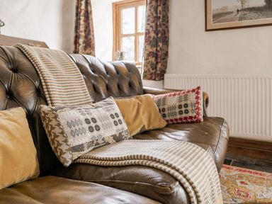 A sofa with cushions and blanket at Cove Cottage in Llangrannog