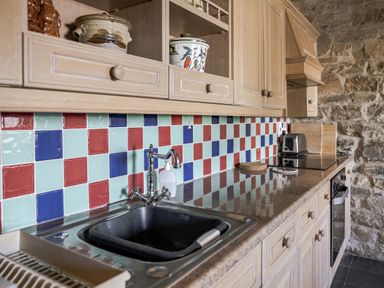 A kitchen with cabinets, a sink, and tiled backsplash at Cove Cottage Llangrannog