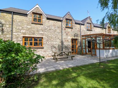 A stone house with wooden windows a patio table and a grassy garden at Y Bwthyn in Llangrannog