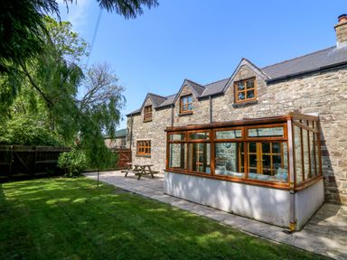 A stone house with a glass conservatory and wooden picnic table in a garden at Y Bwthyn in Llangrannog