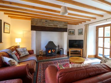 A living room with leather sofas a wood burning stove and a television by a glass door at Y Bwthyn in Llangrannog