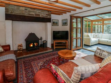 A living room with a wood burning stove two leather sofas a round wooden coffee table and a rug at Y Bwthyn in Llangrannog