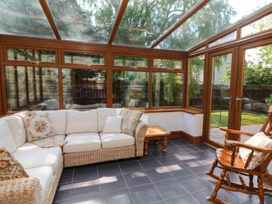 A conservatory with a wicker sofa with cushions a wooden rocking chair and a small wooden table at Y Bwthyn in Llangrannog