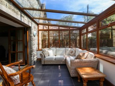 A sunroom with wicker sectional sofa wooden chair and wooden coffee table at Y Bwthyn in Llangrannog