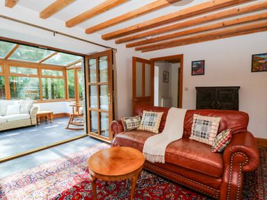 A living room with a leather sofa and wooden coffee table connected to a sunroom with wicker furniture at Y Bwthyn in Llangrannog