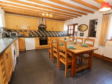 A kitchen with wooden cabinets black tiled floor and a wooden dining table set with plates and glasses at Y Bwthyn in Llangrannog