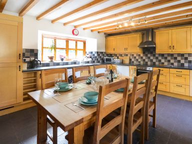 A kitchen with wooden dining table set with plates and glasses and yellow cabinets at Y Bwthyn in Llangrannog