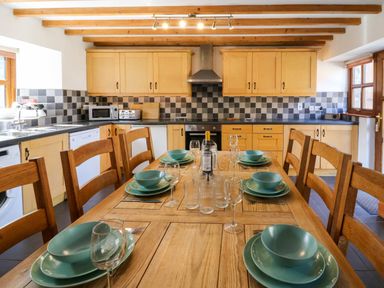 A kitchen with wooden cabinets a dining table set with plates bowls glasses and a bottle at Y Bwthyn in Llangrannog