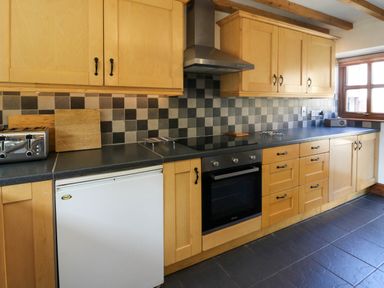 A kitchen with wooden cabinets a black countertop a stove toaster and a window at Y Bwthyn in Llangrannog