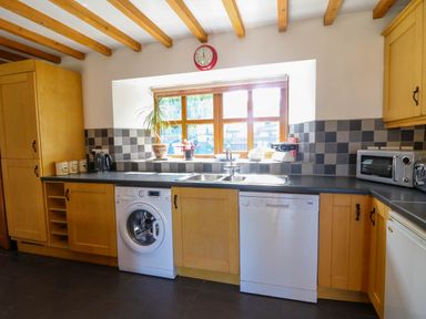 A kitchen with wooden cabinets washing machine dishwasher and window at Y Bwthyn in Llangrannog