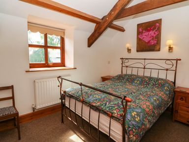 A bedroom with a metal bed frame and butterfly patterned bedspread a wooden chair under a window and two wooden bedside tables with lamps at Y Bwthyn in Llangrannog