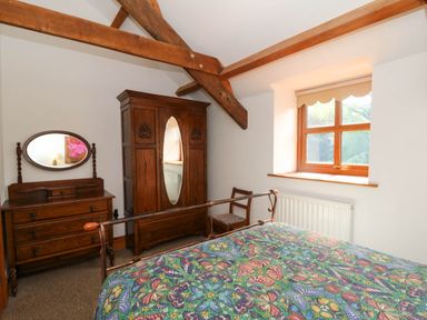 A bedroom with wooden furniture including a wardrobe with a mirror chest of drawers with an oval mirror and a chair by a window at Y Bwthyn in Llangrannog