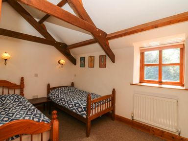 A bedroom with two wooden single beds under wooden ceiling beams and a window with a radiator below at Y Bwthyn in Llangrannog