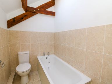 A bathroom with a white toilet and bathtub with beige tiled walls at Y Bwthyn in Llangrannog
