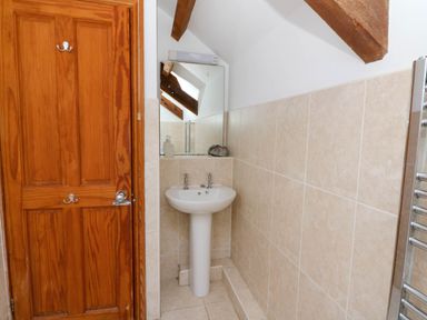 A small bathroom with a wooden door a pedestal sink a mirror and tiled walls at Y Bwthyn in Llangrannog