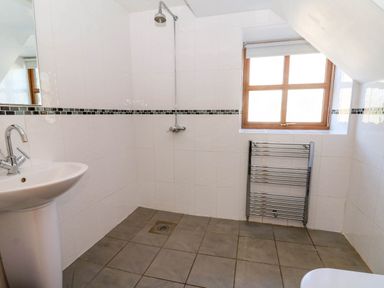 A bathroom with a shower head sink towel radiator and window at Y Bwthyn in Llangrannog