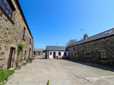 An outdoor courtyard area with stone buildings and a small white building at Y Bwthyn in Llangrannog