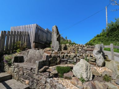 An outdoor stone bench and rock garden with a wooden fence and pathway in the background at Y Bwthyn in Llangrannog