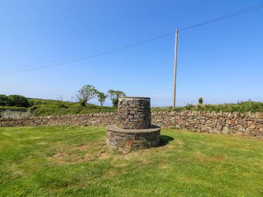 A stone well in a grassy yard surrounded by a stone wall and a wooden utility pole at Y Bwthyn in Llangrannog