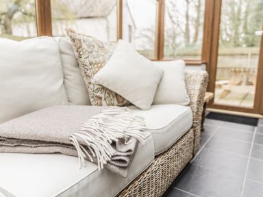 A sofa with cushions and a throw blanket at Y Bwthyn in Llangrannog