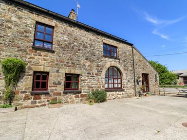 Stone exterior of a house with multiple windows and a paved area in front at Coach House in Llangrannog