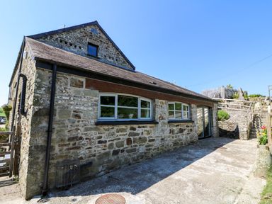 Stone exterior of a building with windows and a wooden staircase leading to an upper area at Coach House in Llangrannog