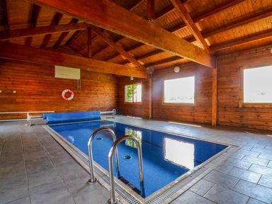 An indoor swimming pool with wooden walls and ceiling and large windows at Coach House in Llangrannog