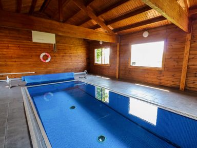 An indoor swimming pool with blue tiles inside a wooden cabin at Coach House in Llangrannog