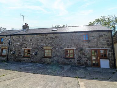 Stone exterior of a long building with multiple windows and a wooden door at Coach House in Llangrannog