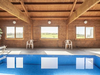 An indoor pool area with windows and plastic chairs at Coach House in Llangrannog