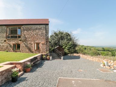 The exterior of a stone building with windows and a gravel driveway with flower pots and a bench at Newlands Barn in Wellington