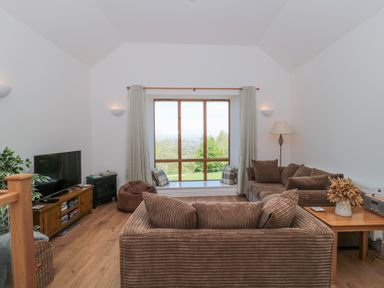 A living room with brown sofas a wooden table a television and a large window at Newlands Barn in Wellington