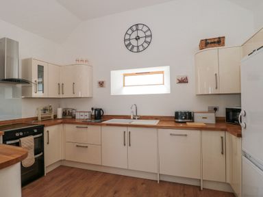 A kitchen with white cabinets wooden countertops a black stove a sink under a small window and various appliances at Newlands Barn in Wellington