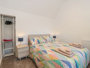 A bedroom with a double bed with colorful quilt and towels on it two bedside tables with lamps and an open wardrobe with hangers and storage box at Newlands Barn in Wellington
