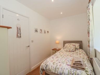 A small bedroom with a single bed a bedside table with a lamp folded towels on the bed and a window with floral curtains at Newlands Barn in Wellington