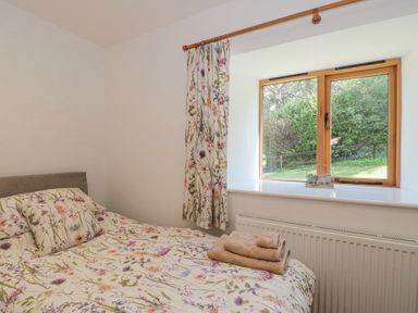 A bedroom with a bed with floral bedding next to a window with matching curtains and folded towels near Newlands Barn in Wellington