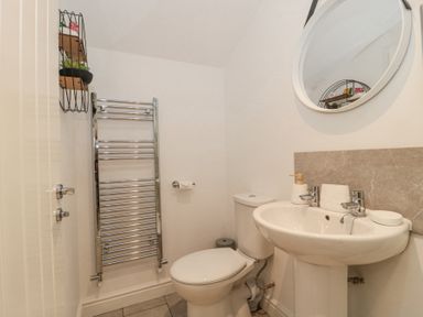 A bathroom with a toilet, pedestal sink, round mirror, towel radiator, and small wall shelf at Newlands Barn in Wellington