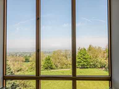 A window with wooden frame showing trees and grassy field outside at Newlands Barn in Wellington