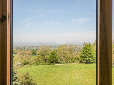 A view of green fields trees and distant hills through a wooden framed window at Newlands Barn in Wellington