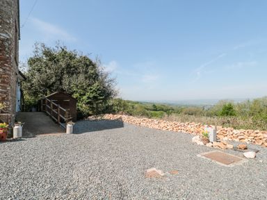 An outdoor gravel area with a wooden shed and stone wall overlooking a green landscape at Newlands Barn in Wellington