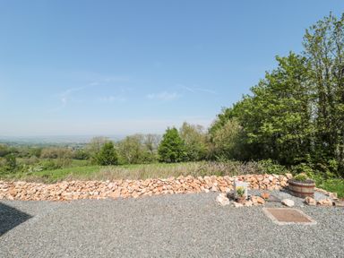 An outdoor area with a gravel ground a low stone wall trees and a wooden planter at Newlands Barn in Wellington
