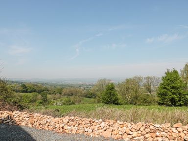 A stone wall with a gravel path in front of a grassy field and trees under a blue sky at Newlands Barn in Wellington